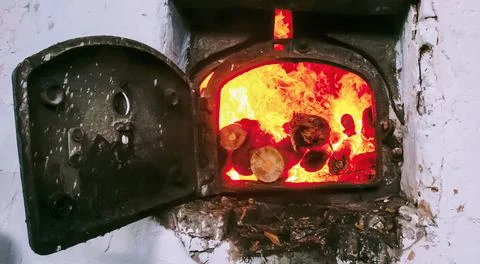 Flickering flames dance inside an old wood-burning stove, casting a warm glow Stock Photos