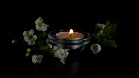 Flickering tea light candle with white spring blossoms on black background 動画素材 334172946