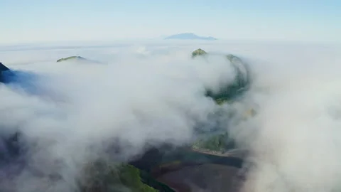 Flight above dense white clouds over dark water with green hills at shoreline Stock Footage 169092739