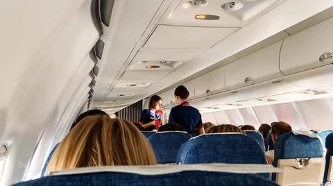Flight attendants in the aisle between the rows of seats serve passengers. Stock Photos