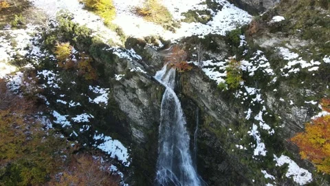 Flight away from a waterfall surrounded by trees with autumn leaves and snow Stock Footage 166199512