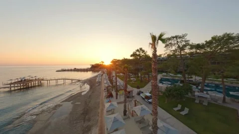 Flight close to Antalya parasol row on resort beach toward glowing sunset; Stock Footage 196993797