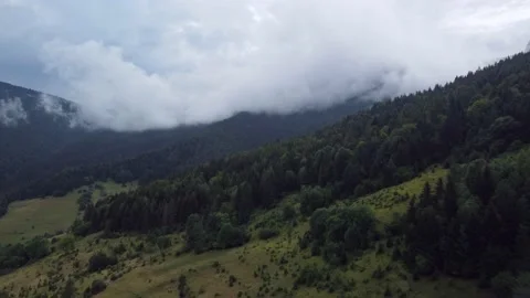 A flight from mountain meadows over green forests, under a misty mountain after Stock Footage 211814262
