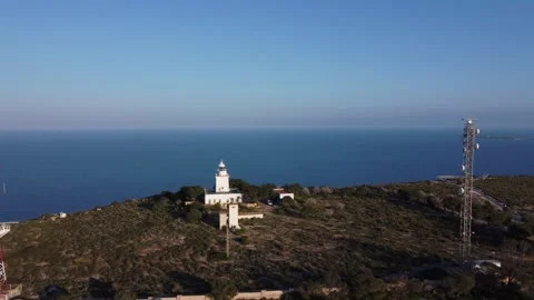 Flight moving away from a lighthouse and radar antennas atop a cliff in the Video stock 333625591