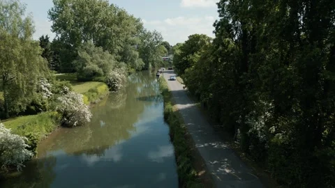 Flight moving forward over over a canal calm waters green banks with a road Stock Footage 296820227