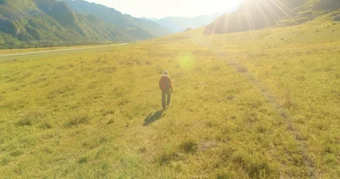 Flight over Backpack hiking tourist walking across green mountain field. Huge Stock Footage 115099962