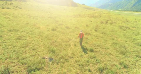 Flight over Backpack hiking tourist walking across green mountain field. Huge Stock Footage 129282928