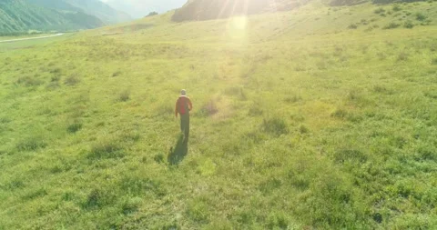 Flight over Backpack hiking tourist walking across green mountain field. Huge Stock Footage 165569162