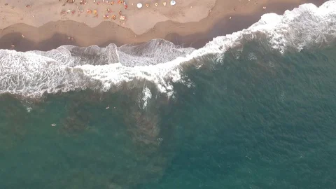 Flight over the blue ocean with big waves and people sunbathing under umbrellas 库存影片 129517706