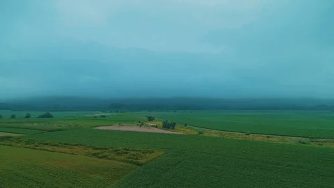 Flight over crop fields and rugged road at the bottom of a mountains in mist at Stock Footage 124028516