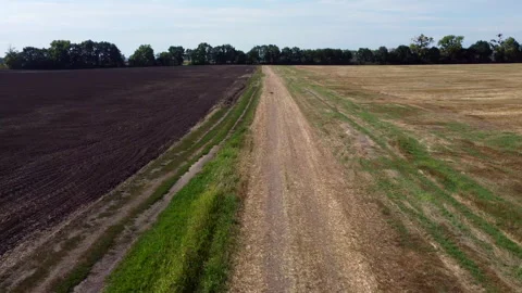 Flight over dirt road between field plowed earth field after straw harvesting Stock Footage 256031831