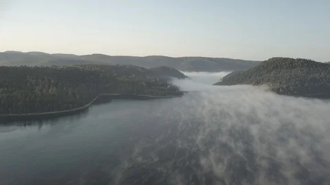 Flight over a lake and dam surrounded by mountains with some mist 4k ungraded Stock Footage 105830403