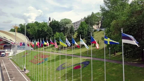 Flight over a large number of flags in a row fluttering in the wind in city park Stock Footage 136734109