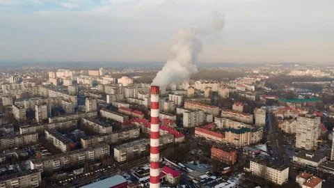 Flight over a red-white pipe and smoke pouring out of it onto the city block.  Stock Footage 102699340