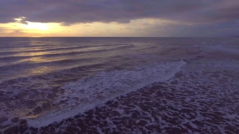 Flight over the sea with foam waves at sunset, in the background a coastline and Stock Footage 73604809