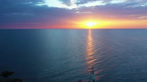 Flight over a sunny path to a lighthouse on an island and a beautiful sunrise Stock Footage 176480474