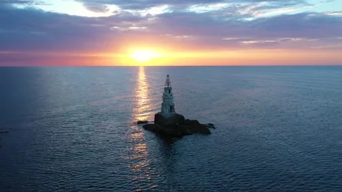 Flight over a sunny path to a lighthouse on an island and a beautiful sunrise Stock Footage 254356195