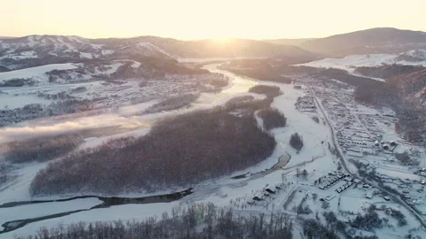 Flight over the winter river in the mountains. Beautiful sunrise from behind the Stock Footage 136872099