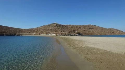 Flight over yellow sand Kolona beach line towards mountain with white church Stock Footage 86972644