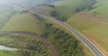 Flight round the bend in road and rail tracks next to river in green valley Stock Footage 85956911