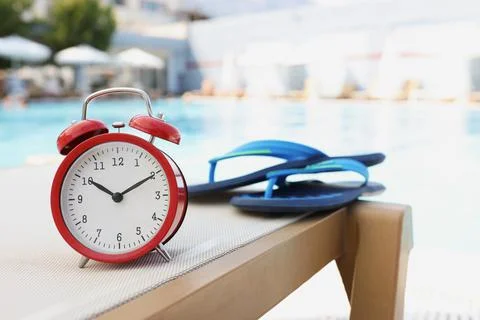 Flip flops alarm clock on deck chair by pool Foto stock