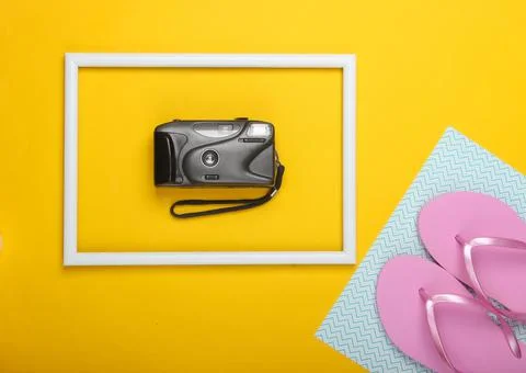 Flip flops and retro camera on yellow background with white frame. Studio sho Фото