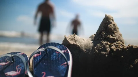 Flip Flops on the Beach. Behind two Men in the Ocean on Sunny day 스톡 동영상 112896367
