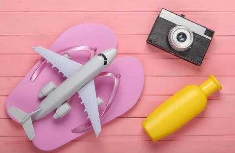 Flip flops with a camera, plane, sunblock on a pink wooden background. Beach  Фото