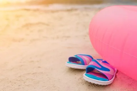 Flip-flops lying on beach under pink swimming circle. Summer vacation concept Stockfoto's