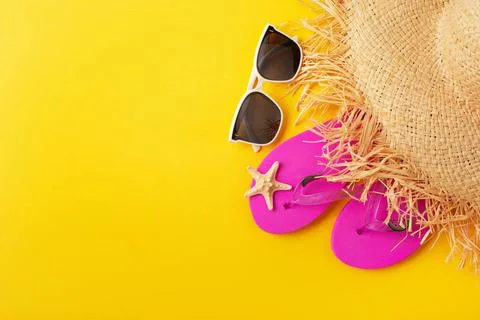 Flip flops straw hat sunglesses and starfish on yellow background vacation... Stock Photos