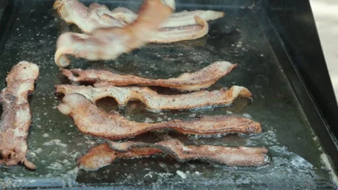 Flipping bacon cooking on a flat top grill outside Stock Footage 311203867