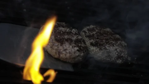 Flipping Two Tall Raw Meat Burgers on a Fire Grill Stock Footage 129044817