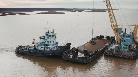 A floating barge with a pile of sand held by a tugboat. The bucket of the crane Stock Footage 217406540