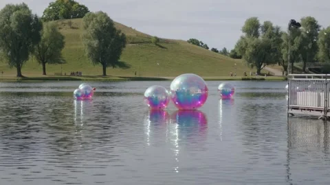 Floating Colored Spheres on Quiet Park Lake, Willow Trees and Hill, Medium Shot Stock Footage 343024623