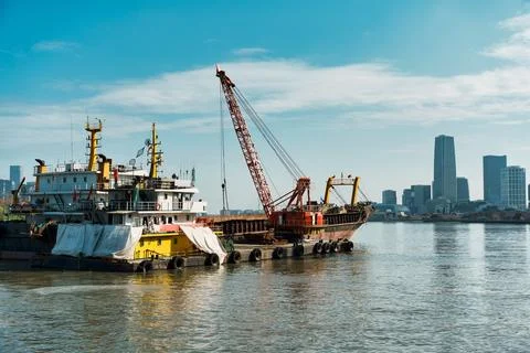Floating Crane Barge and Cargo Ship on River With City Skyline Background 写真素材