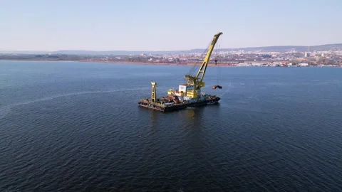 A floating crane barge with a large yellow crane operates on calm waters Stock Footage 303511107