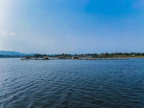 Floating fish cages and small huts on a calm lake under a clear blue sky 写真素材