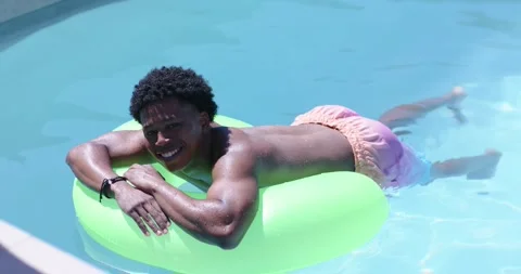 Floating male lying on green inflatable ring in residential pool, wearing pink Stock Footage 334925155