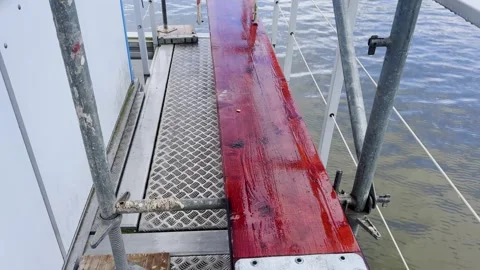 Floating platform walkway with a wet red wooden plank, metal grating floor Stock Footage 341427011