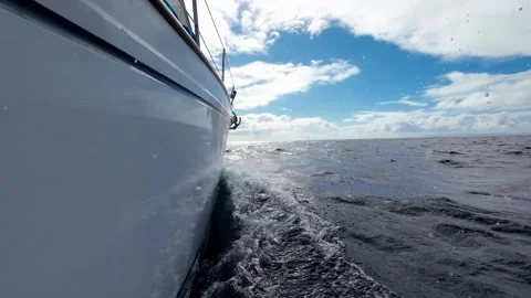 Floating sailing yacht with spread sails splitting the sea waves and an island Stock Footage 282661628