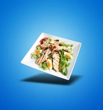 Floating White plate with Caesar salad  on blue gradient Stock Photos