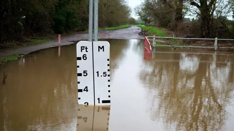 Flood level indicator marking rising water on submerged rural roadway. Brown Stock Footage 329770777