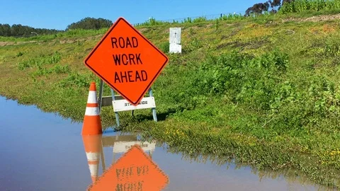 Flooded area with 'road work ahead' sign and orange reflector cone. 库存影片 106011878