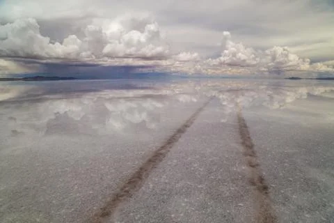 Flooded salt flats with reflection of clouds in the water and a car track cro Stock Photos
