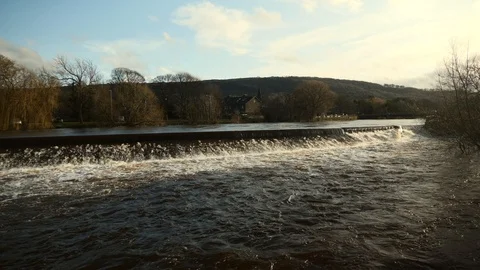 A flooded UK river creating a heavy waterfall downstream. Vídeo Stock 125586871