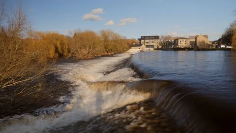 A flooded UK river creating a heavy waterfall downstream. Vídeo Stock 125586931