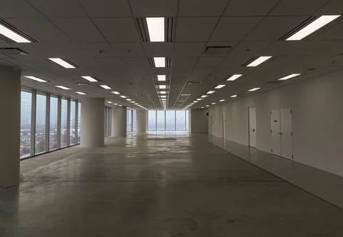 Floor-to-ceiling windows frame a panoramic city skyline view in a large, em.. 写真素材
