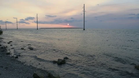 Florida Keys sunset with pink sky, power lines, green water, dark rocky beach Stock Footage 92763380