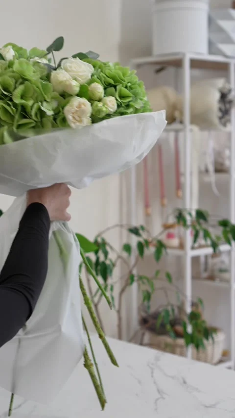 A florist adjusts the white packaging on a white and green bouquet of roses, hyd Stock Footage 317961636