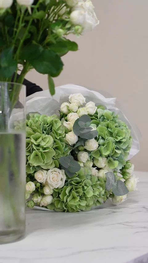 A florist adjusts the white packaging on a white and green bouquet of roses, hyd Stock Footage 317961651